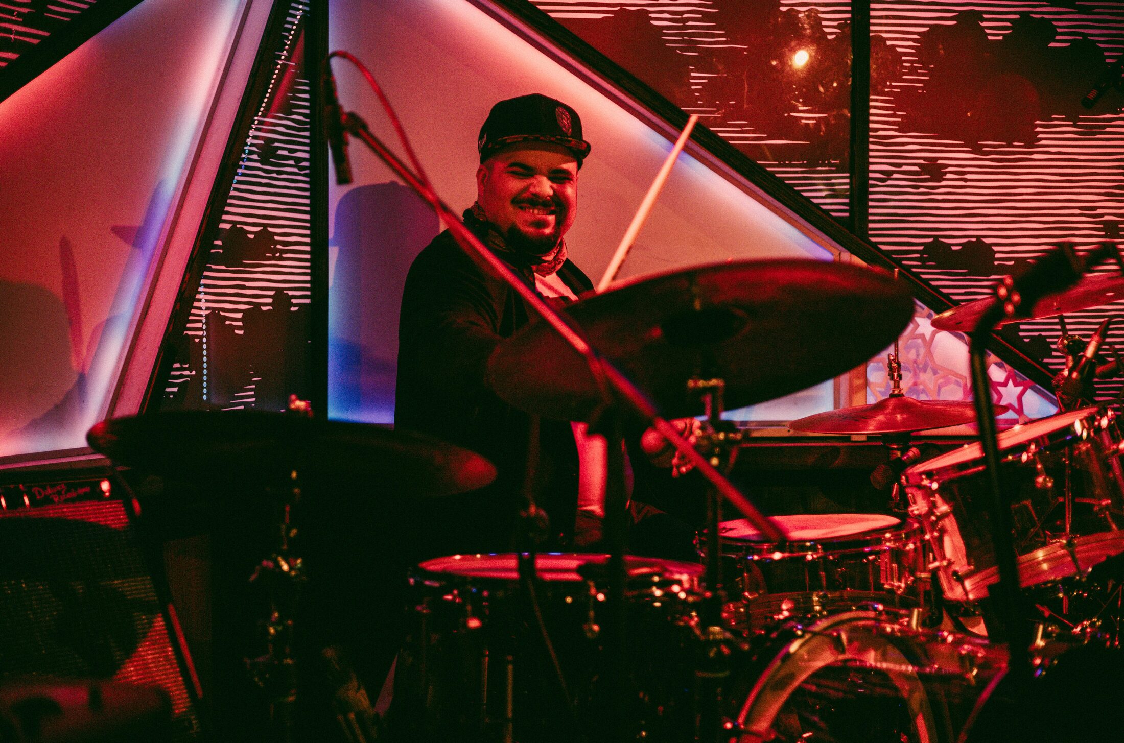 Ben Silashi smiling behind the drums in red light